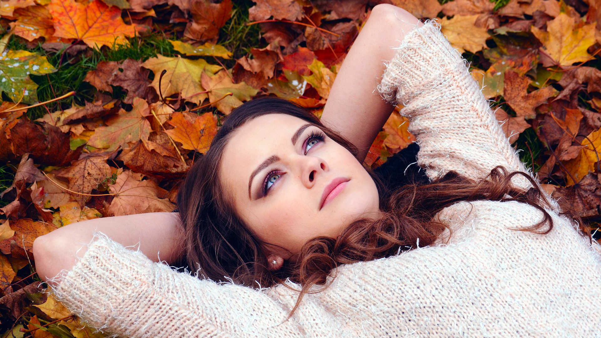 Herfst - vrouw ligt tussen de bladeren en kijkt de hemel